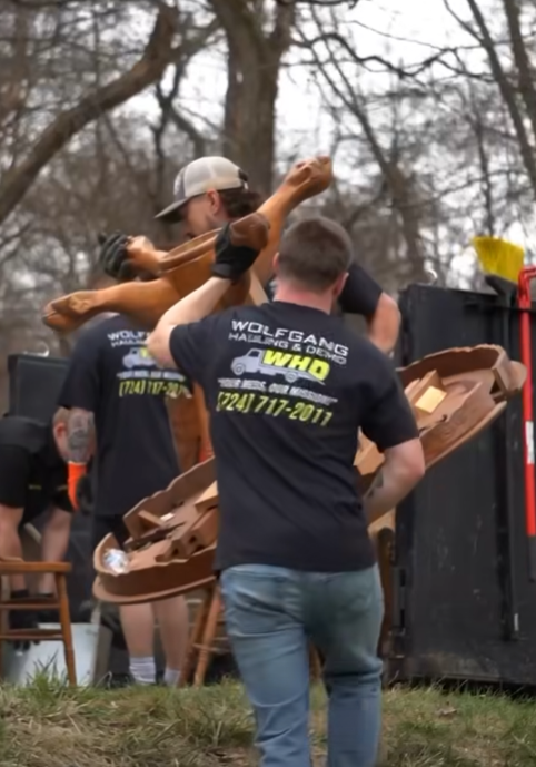 Wolfgang Hauling crew member in a branded shirt tossing debris into the truck